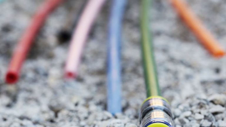 Ein Bündel farbiger Kabel oder Schläuche liegt auf einem Kiesbett. Die Enden der Kabel oder Schläuche sind verschiedenfarbig und im Vordergrund befindet sich einer mit gelber Umrandung.