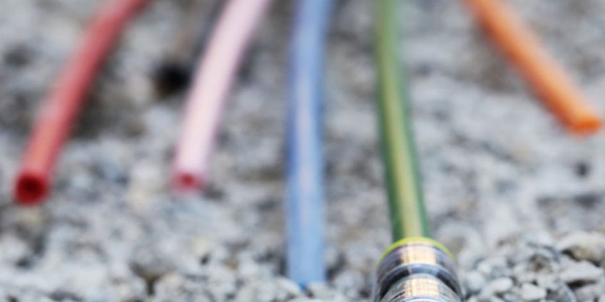 Ein Bündel farbiger Kabel oder Schläuche liegt auf einem Kiesbett. Die Enden der Kabel oder Schläuche sind verschiedenfarbig und im Vordergrund befindet sich einer mit gelber Umrandung.