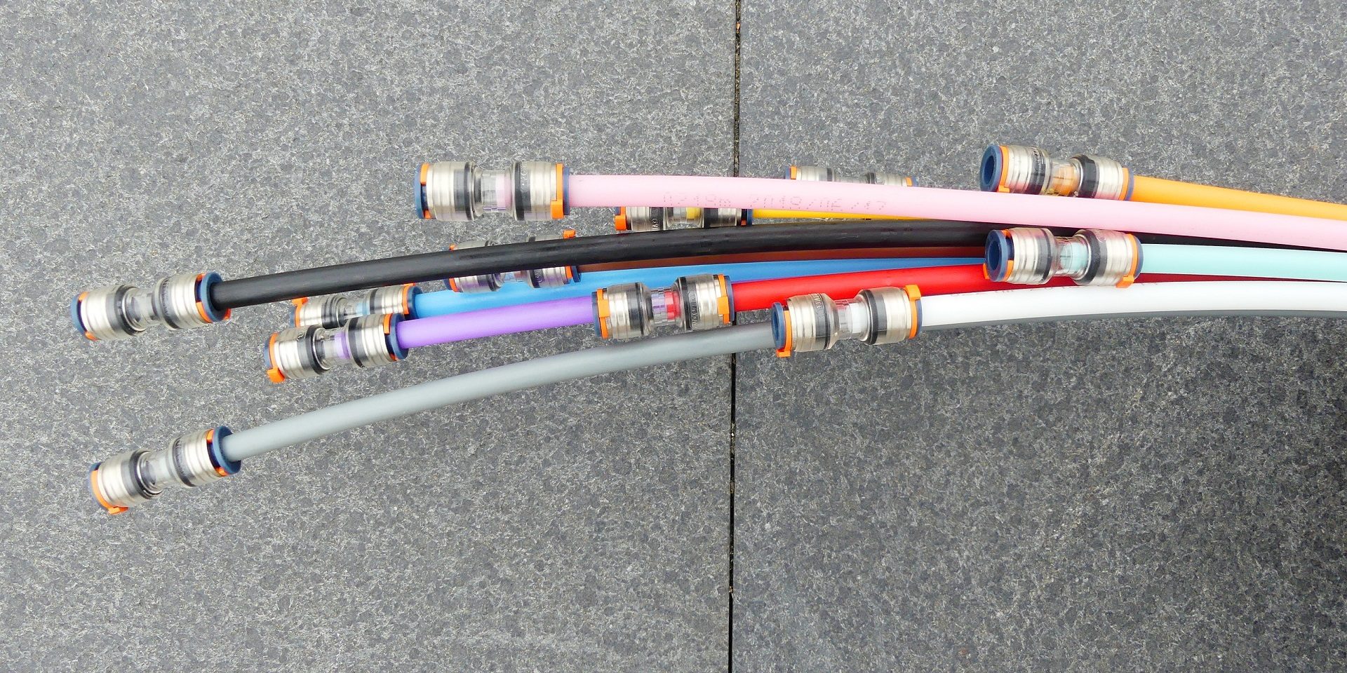 Mehrere bunte Kabel mit Metallverbindern ragen nach rechts aus dem Bild. Der Hintergrund besteht aus einer grauen, strukturierten Steinfläche.