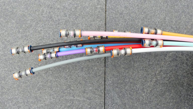 Mehrere bunte Kabel mit Metallverbindern ragen nach rechts aus dem Bild. Der Hintergrund besteht aus einer grauen, strukturierten Steinfläche.