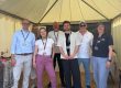 Eine Gruppe von sieben Personen steht unter einem weißen Pavillon mit der Aufschrift „BKZ.SH, ZVO & LAND SH“. Sie lächeln und tragen Namensschilder. Im Vordergrund sind Holzboden und ein Tisch mit Broschüren zu sehen.