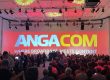 Eine große Konferenzhalle mit vielen sitzenden Personen. An der Vorderseite ist eine riesige Projektionswand zu sehen, die mit "ANGACOM" in großen Buchstaben und dem Slogan "Where Broadband Meets Content" beleuchtet ist.