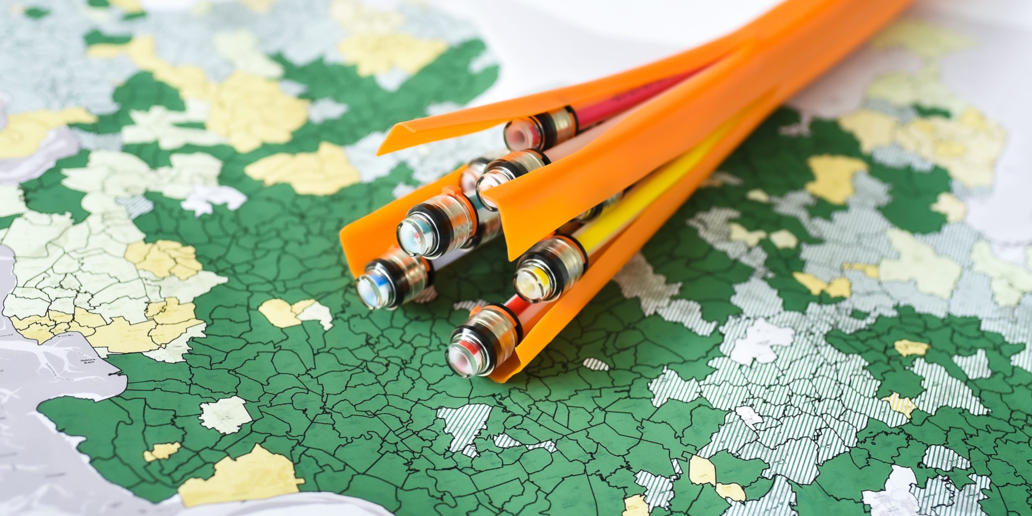 KT7 0501 Mehrere orangefarbene, geöffnete Rohre mit bunten Kabeln darin liegen auf einer Karte. Die Karte zeigt unterschiedliche Regionen in Grün- und Gelbtönen, die an politische oder geografische Grenzen erinnern.