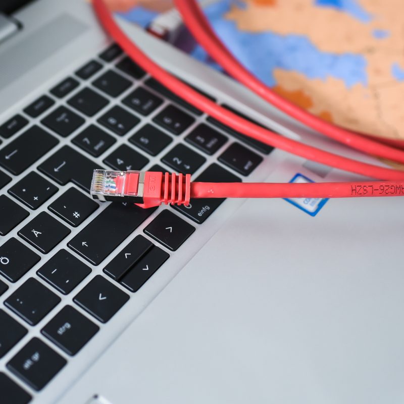 Ein rotes LAN-Kabel liegt auf einer silbernen Laptop-Tastatur. Das Kabel ist teilweise aufgerollt, und der Laptop steht auf einem bunten Untergrund.