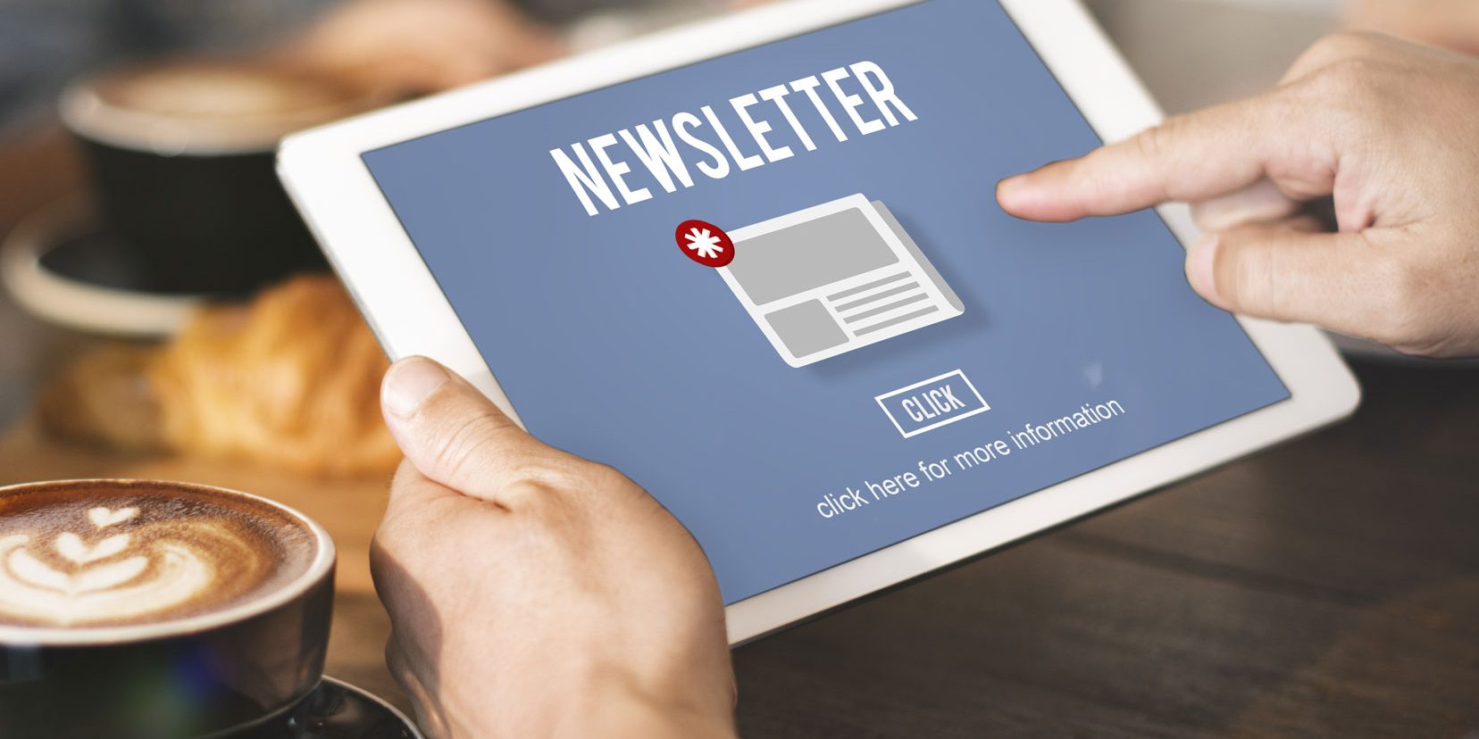 Eine Person hält ein Tablet in der Hand. Auf dem Bildschirm steht "Newsletter" mit einem Symbol für eine Benachrichtigung. Darunter befindet sich ein Button mit der Aufschrift "Click" und einem Hinweis zur weiteren Information. Im Hintergrund sind unscharfe Objekte.